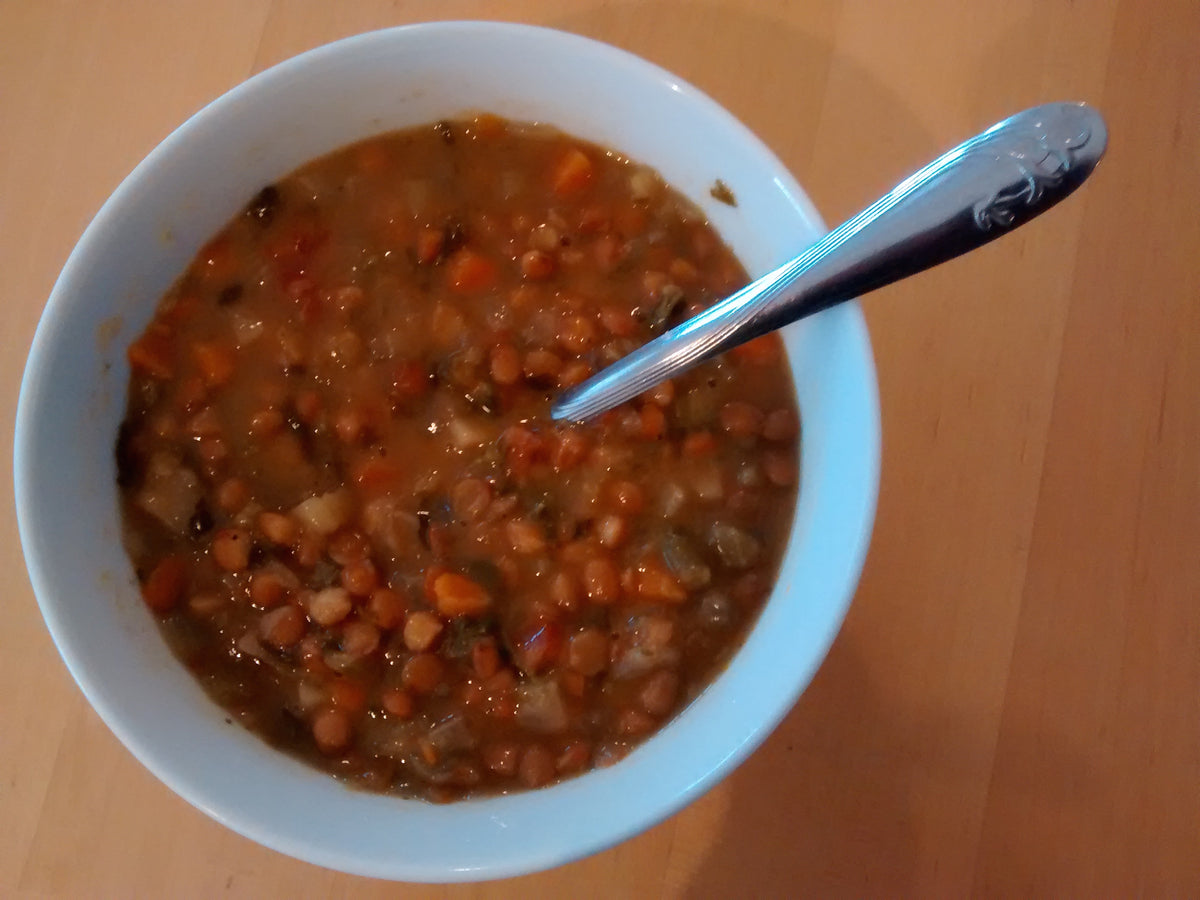 A bowl of lentil and vegetable soup with carrots and greens