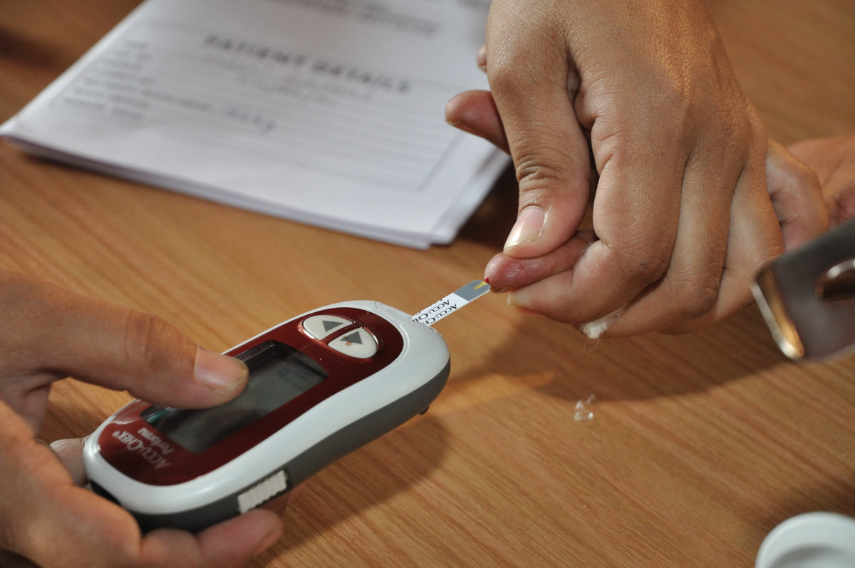 A health worker touches a test strip in a glucose meter to a drop of blood on a fingertip