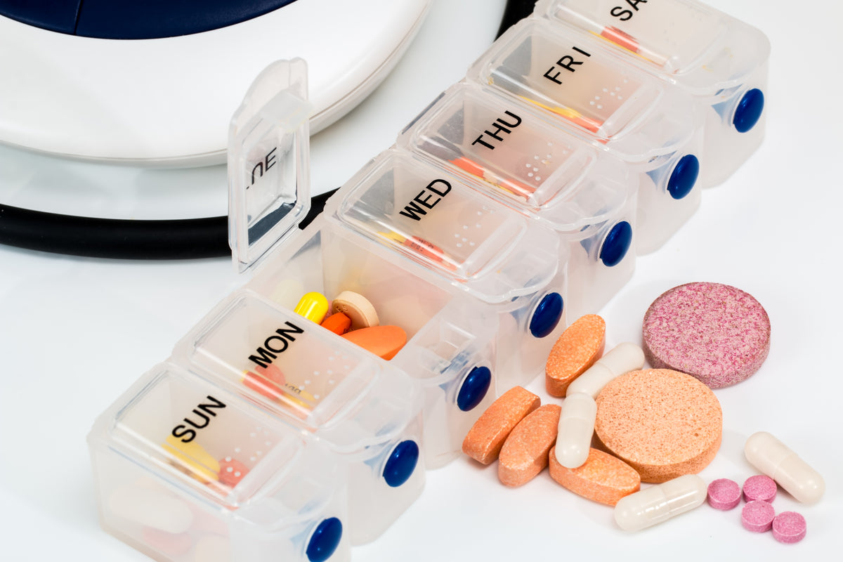 A weekly pill organizer with open compartments holding colorful vitamins and capsules