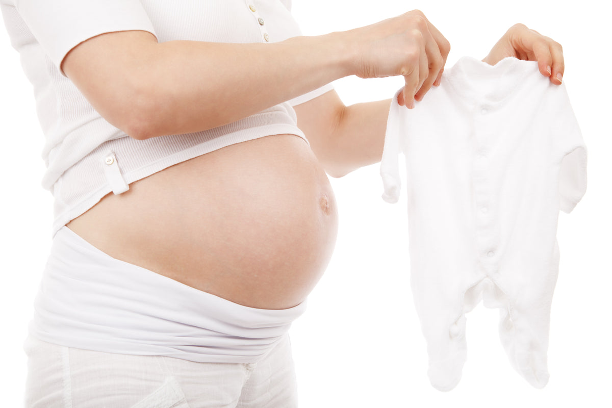 A pregnant woman holding a small white baby sleeper in front of her belly