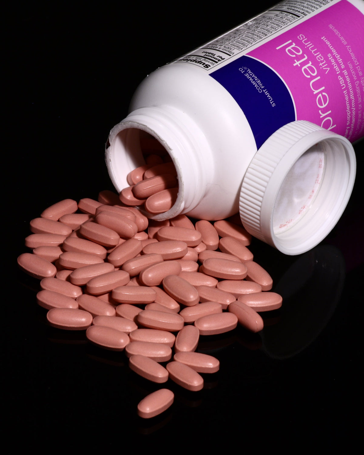Pink prenatal vitamin tablets spilling out of an open bottle