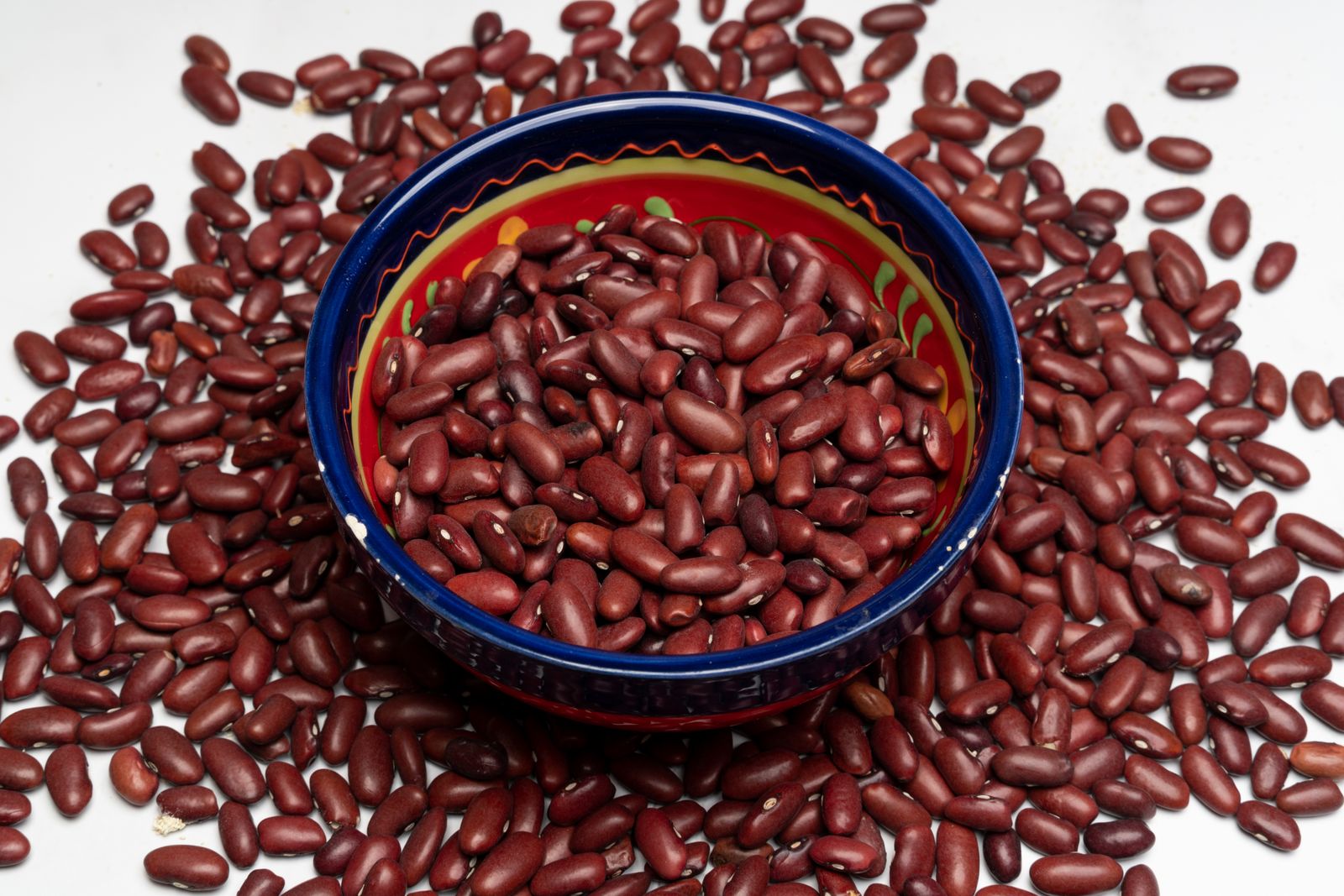 Dried red kidney beans in a blue ceramic bowl surrounded by scattered beans, a high-fiber legume