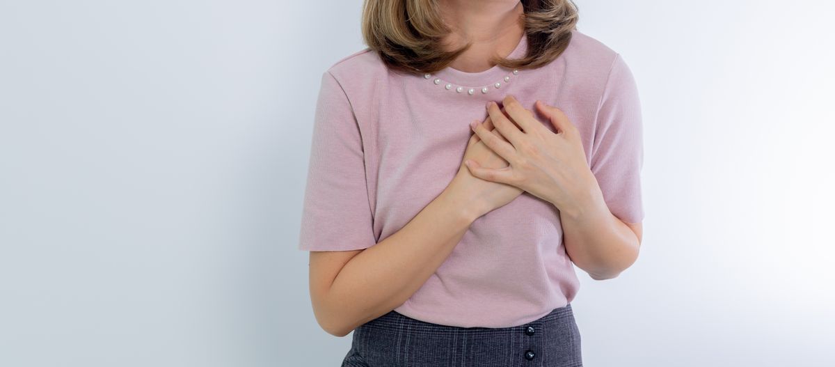 Woman with both hands pressed to her chest against a plain background