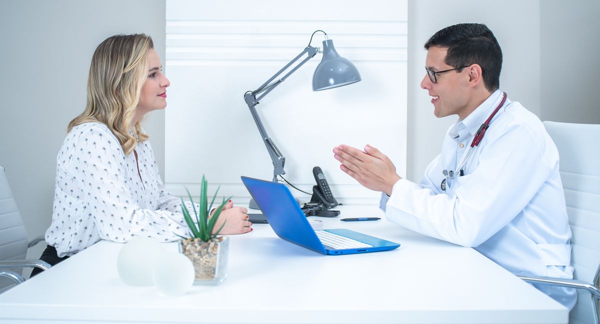 Doctor talking with a woman across a desk in a bright office